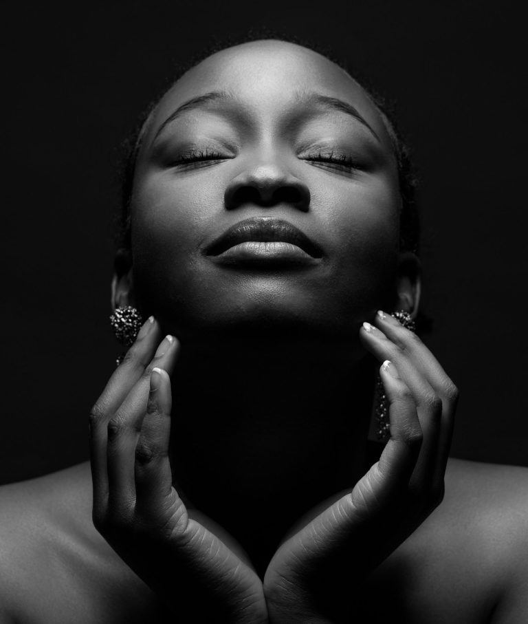 Porträt einer Frau mit geschlossenen Augen, die ihre Hände sanft ans Gesicht hält.
